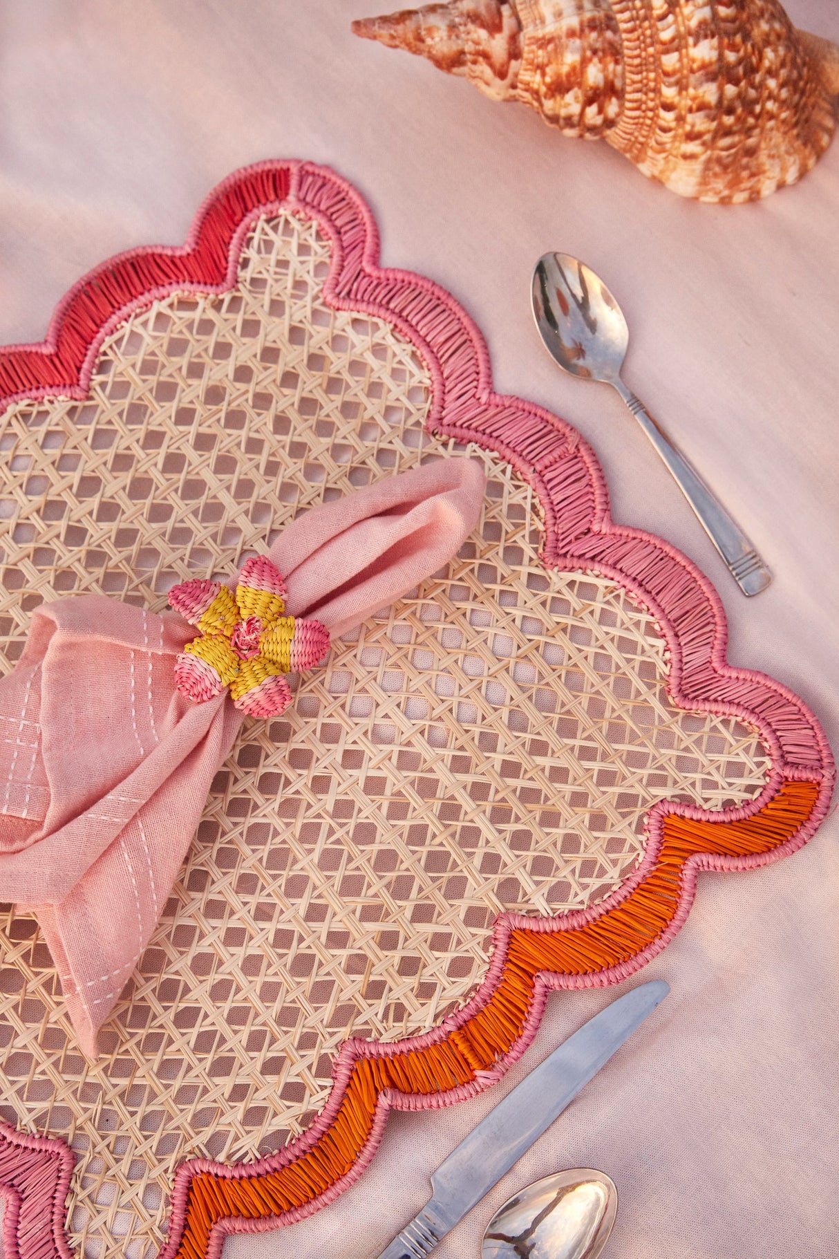 Decorative placemat with pink napkin and floral napkin ring on a pink surface.