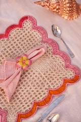 Decorative placemat with pink napkin and floral napkin ring on a pink surface.