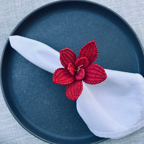 Red floral napkin ring on a white napkin on a blue plate with a gray background