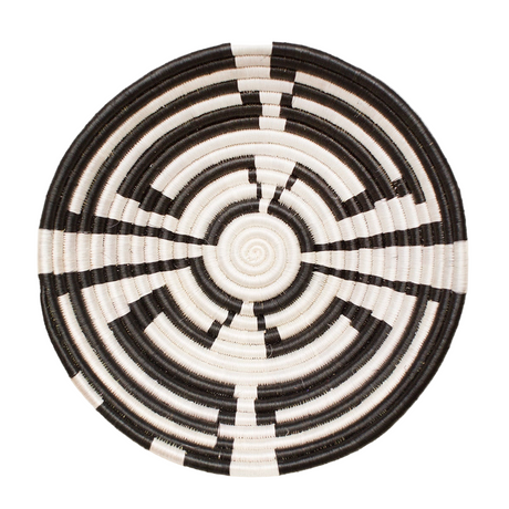 Round woven basket with black and white spiral pattern on a light beige background