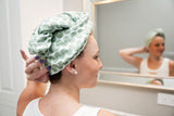 Woman using a green patterned hair towel in front of a mirror.