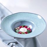 Blue ceramic bowl with a dish of pink noodles and green leaves on a white background
