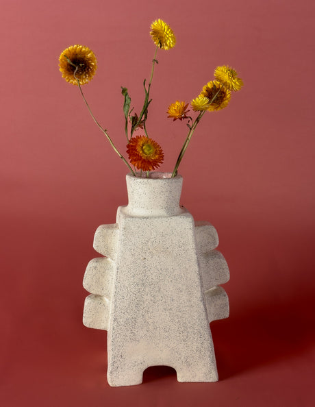Concrete vase with stacked design holding flowers against a red background