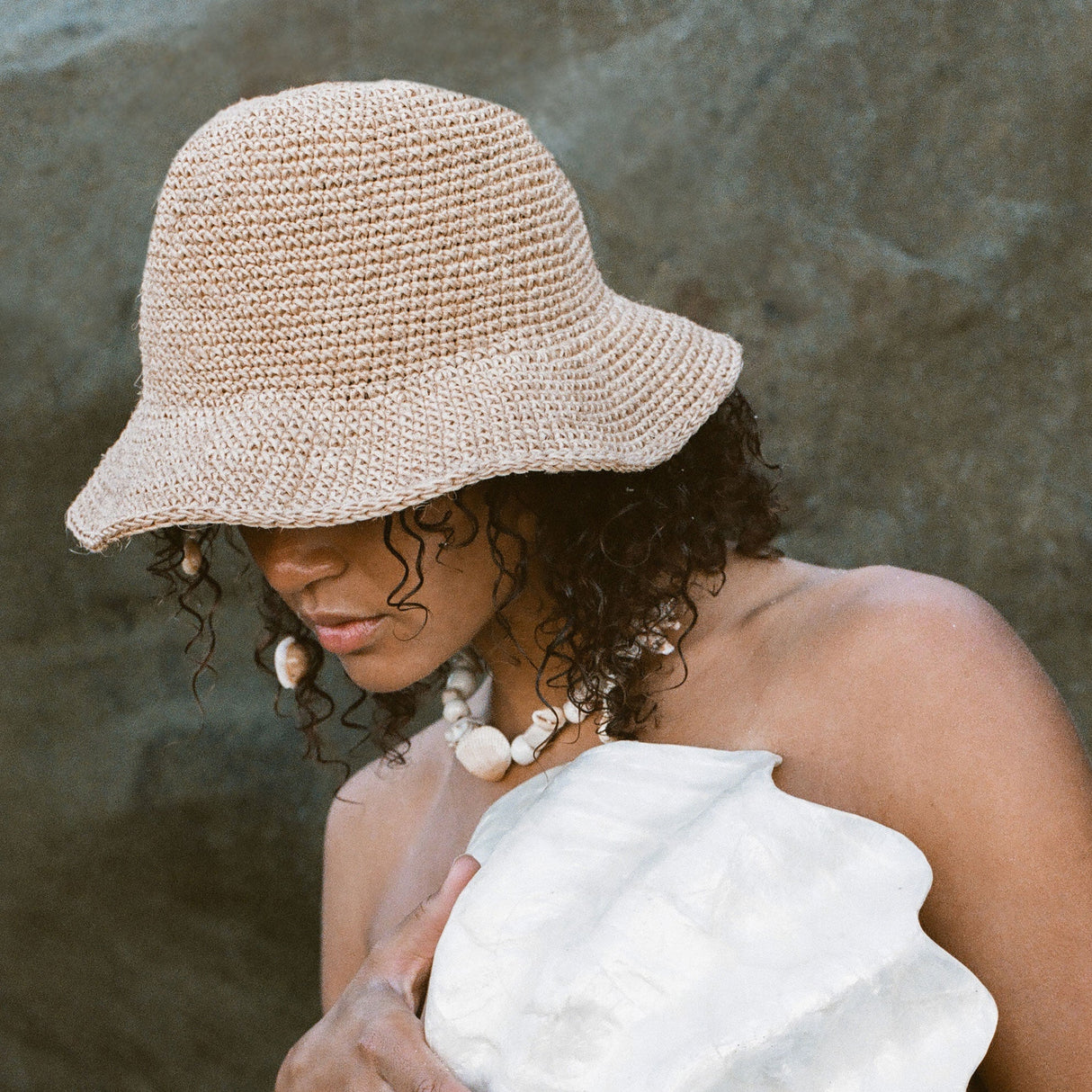Woman wearing a beige woven hat and white top against a neutral background