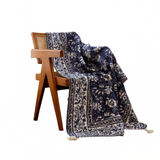 Navy floral patterned throw blanket draped over a wooden chair on a white background