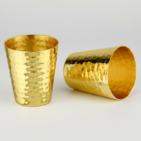 Two gold hammered shot glasses on a light gray background