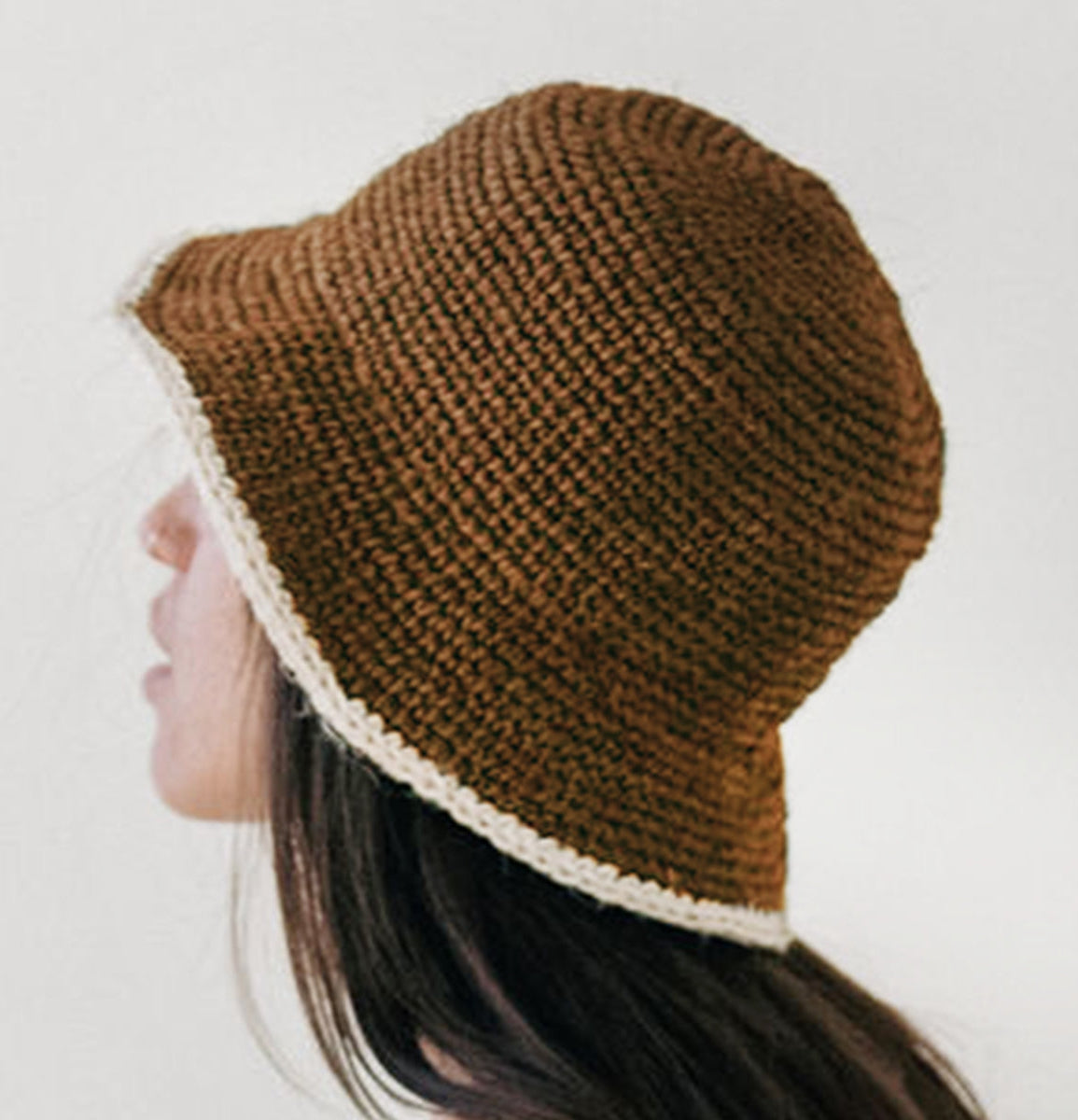 Brown knitted hat with white trim worn by a person on a plain background