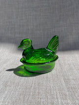 Green glass hen-shaped container  on a gray fabric background