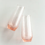 Two clear glass vases with pinkish tint on a light gray background