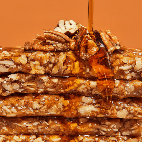 Stack of nutty bars with a drizzle of honey on an orange background