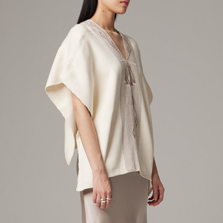 Woman wearing a beige poncho against a gray background