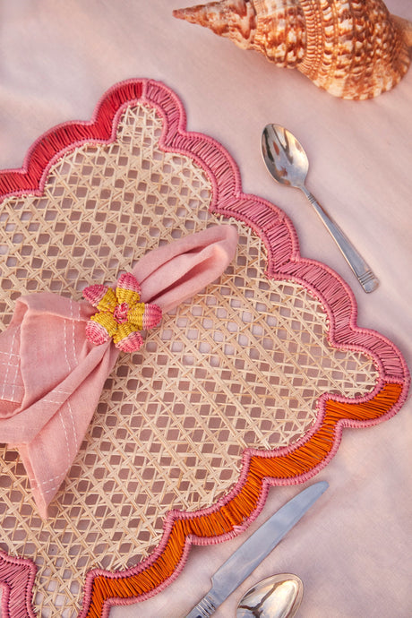 Decorative placemat with pink napkin and floral napkin ring on a pink surface.