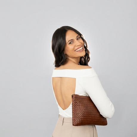 Woman holding a brown clutch against a green and beige background