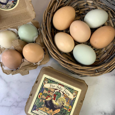Eggs in a cardboard carton and wicker basket with a 'Fire Lake Farm' label on a marble surface.