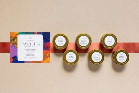 Set of six small candles with labels on a beige surface, accompanied by a colorful card. 2oz Mini Tins 6 Count