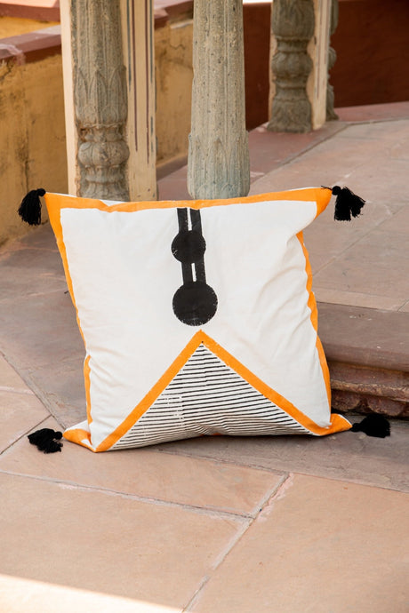 Decorative pillow with orange border and black tassels on a stone floor.