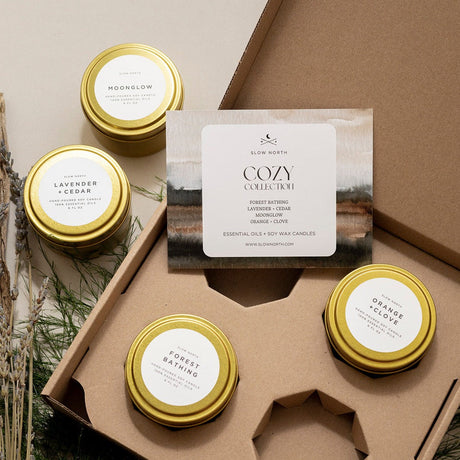 Set of candles in gold tins with labels on a brown box, featuring the 'Cozy Collection' by Slow North.