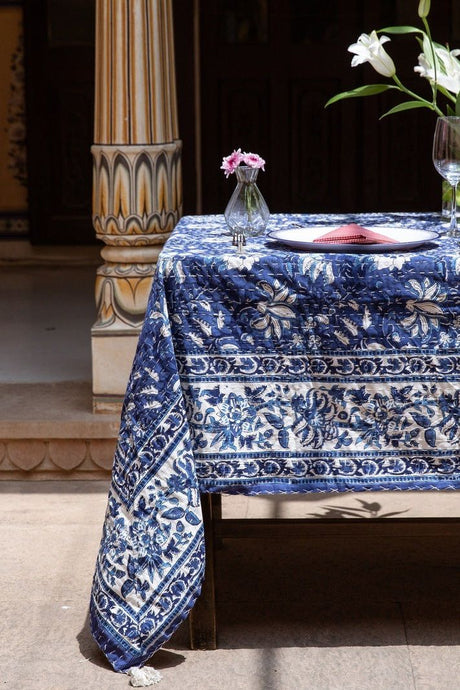 Table with a blue and white patterned tablecloth, vase with flowers, and wine glass.