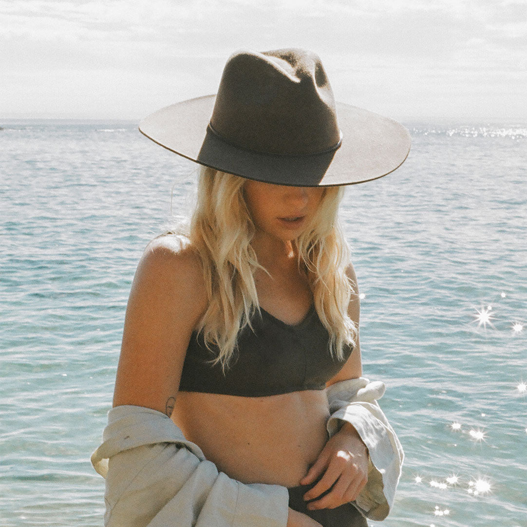 Woman wearing a black hat and black bikini top by the water