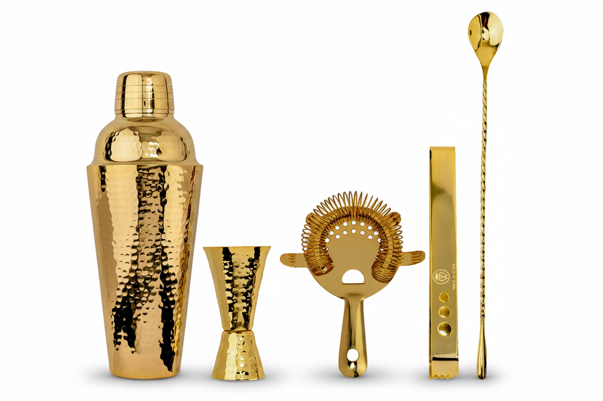 Set of gold cocktail-making tools including a shaker, jigger, strainer, and spoon on a white background.