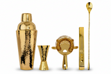 Set of gold cocktail-making tools including a shaker, jigger, strainer, and spoon on a white background.