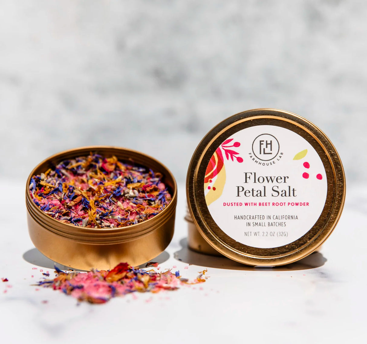 Gold tin of Flower Petal Salt with colorful petals and brand label on a light background