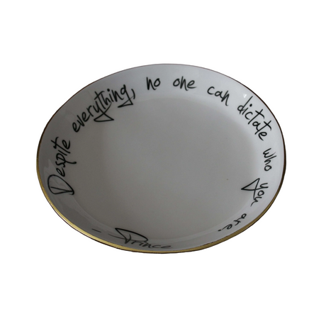 A white ceramic bowl with a gold rim, featuring black handwritten text and signature that reads 'Despite everything, no one can dictate who you are' with a '-Prince-' signature.