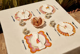 Dining table set with plates, glasses, and cutlery on a white tablecloth.