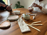 Ceramic utensils and containers on a wooden table with a person in the background.