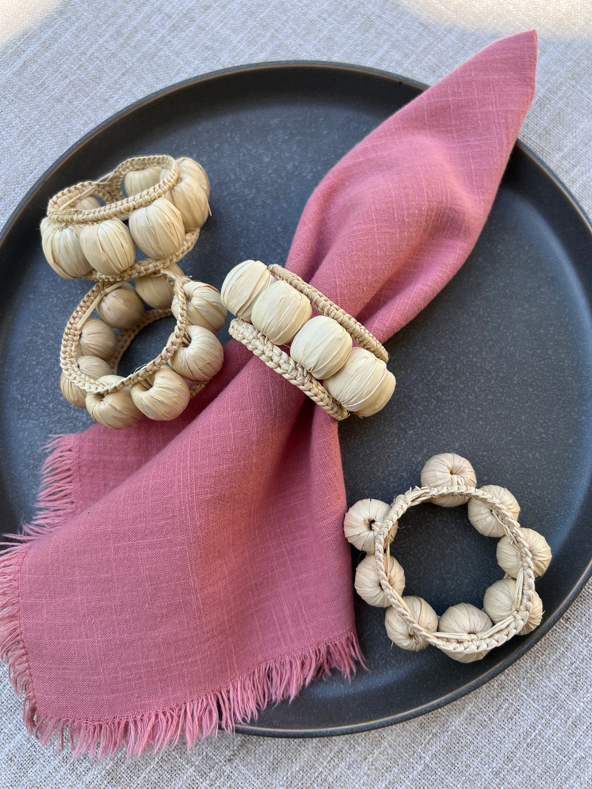 Napkin rings with wooden beads on a pink napkin on a dark plate.