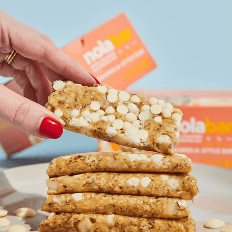 Stack of white chocolate chip cookies with a hand holding one above them, against a light blue background.