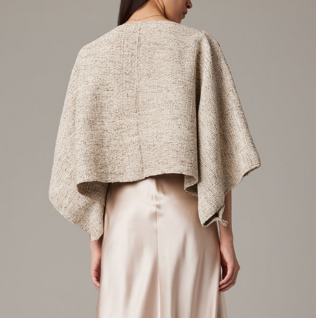 Person wearing a beige knitted shawl over a plain background