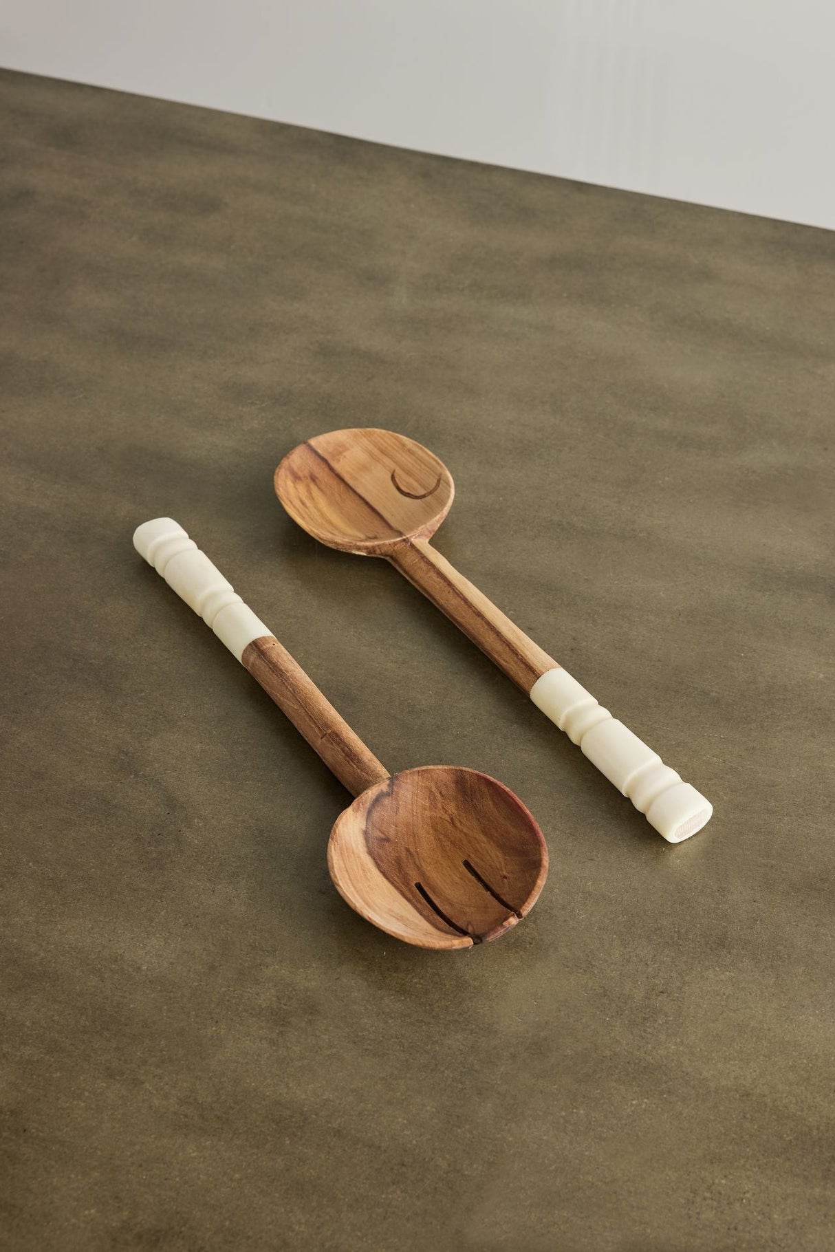 Two wooden ladles with white handles on a brown surface