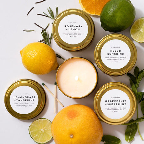 Collection of candles with labels surrounded by citrus fruits and herbs on a light background