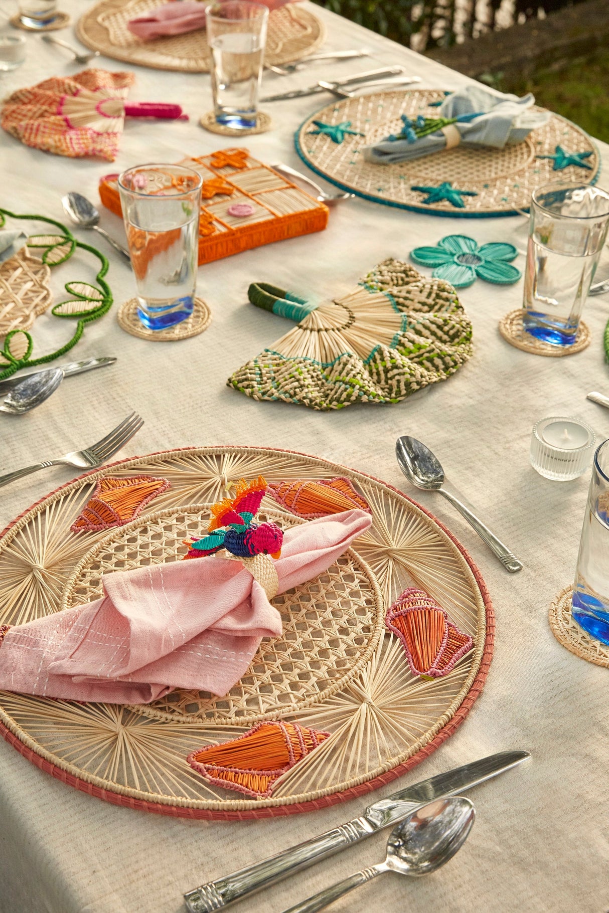 Decorative table setting with wicker placemats, colorful napkins, and cutlery on a light surface.