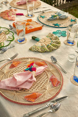 Decorative table setting with wicker placemats, colorful napkins, and cutlery on a light surface.