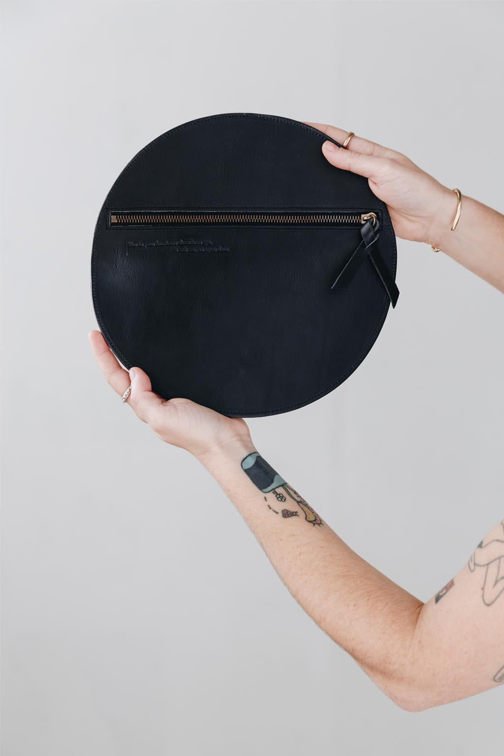 Person holding a black round pouch with a zipper on a light gray background