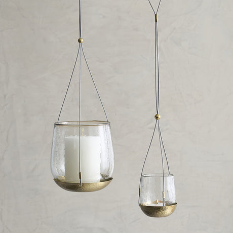 Two hanging glass candle holders with gold accents on a neutral background
