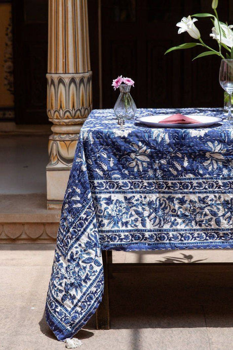 Table with a blue and white patterned tablecloth, vase with flowers, and wine glass.