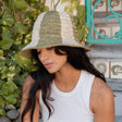 Woman wearing a straw hat in a natural setting with greenery and a decorative metal gate.