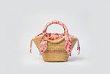 Woven handbag with a pink floral scarf on a light gray background