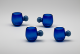 Four blue glass tumblers with spherical handles on a light gray background