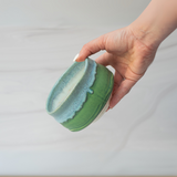 A hand holds the Iguchi Deep Sea Clay Matcha Bowl, showcasing its green and blue Minoyaki pottery design against a softly blurred background.