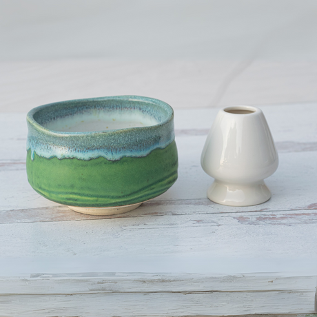 An Iguchi Deep Sea Clay Matcha Bowl and a small white vase grace the light wooden surface.