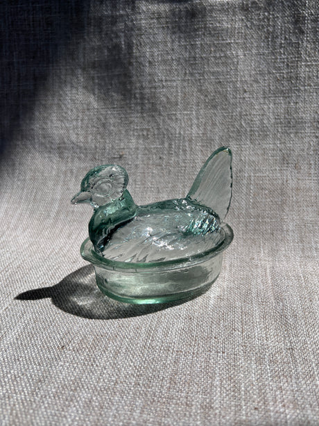 Glass object resembling a nesting hen on a textured fabric background