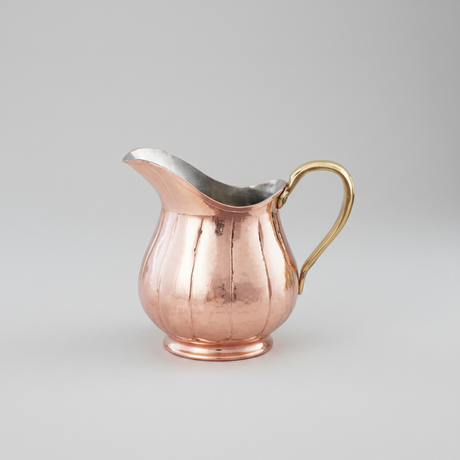 Copper creamer with a gold handle on a white background