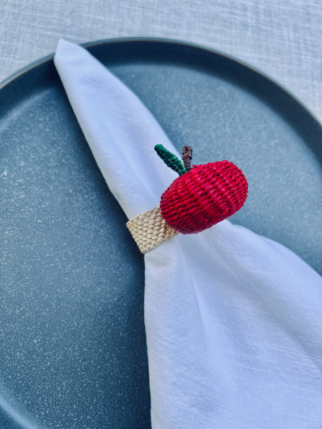 Crocheted apple napkin ring on a white napkin with a blue plate background