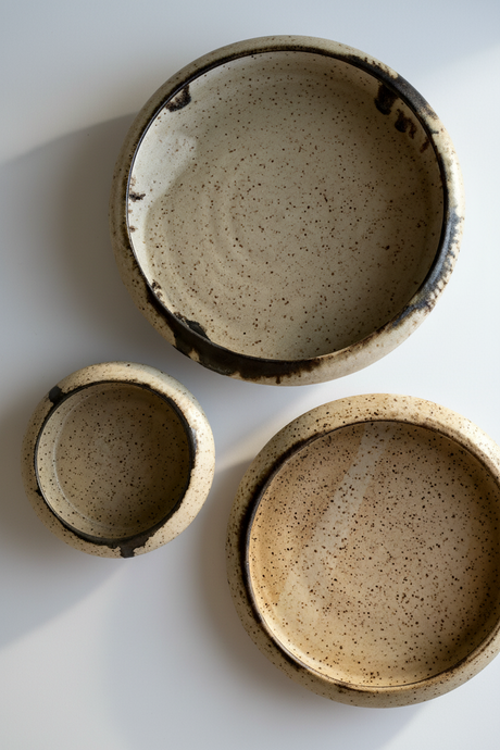 Three ceramic bowls with speckled glaze on a white background
