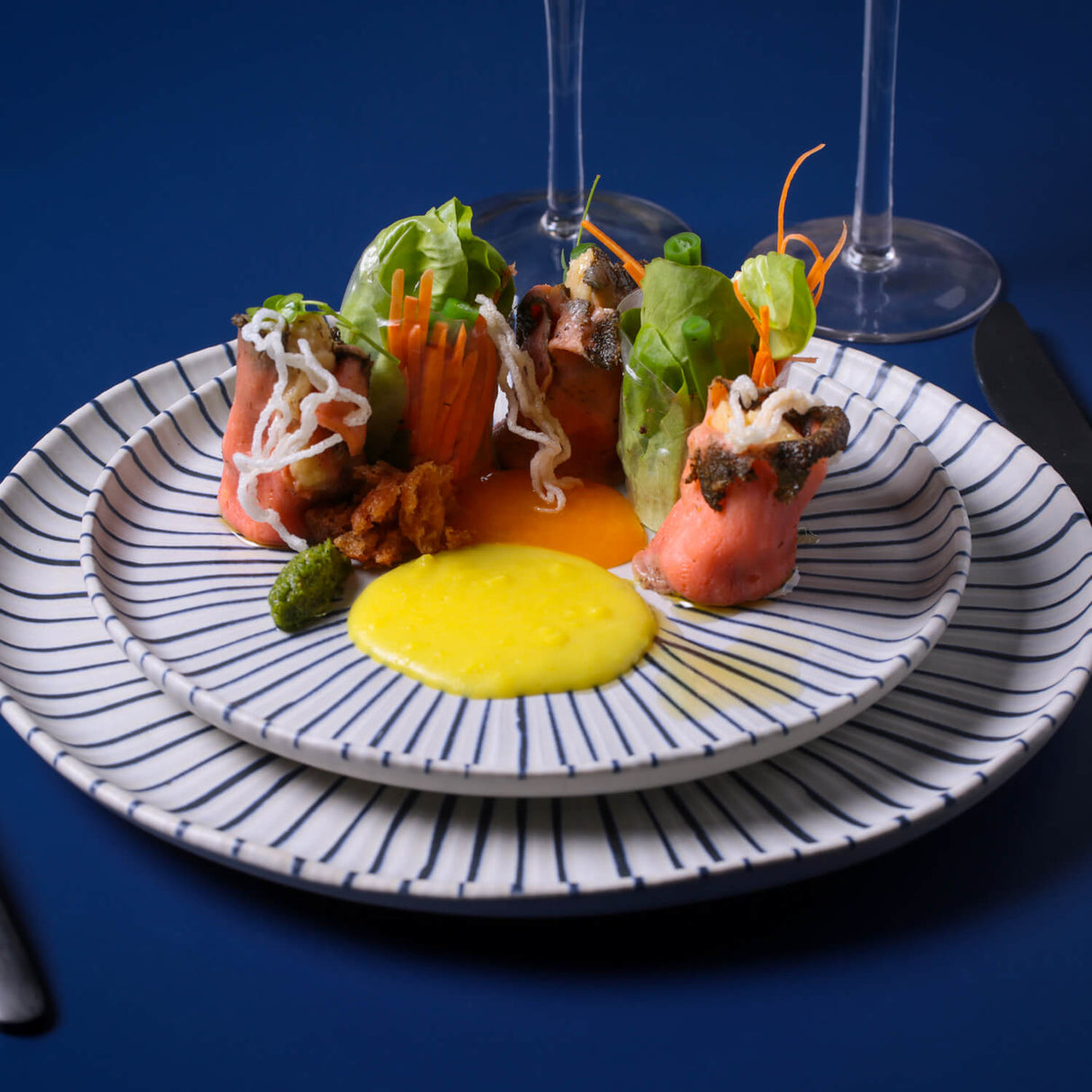 Gourmet dish with seafood and vegetables on a striped plate against a blue background