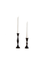 Two white candles in black candle holders on a white background